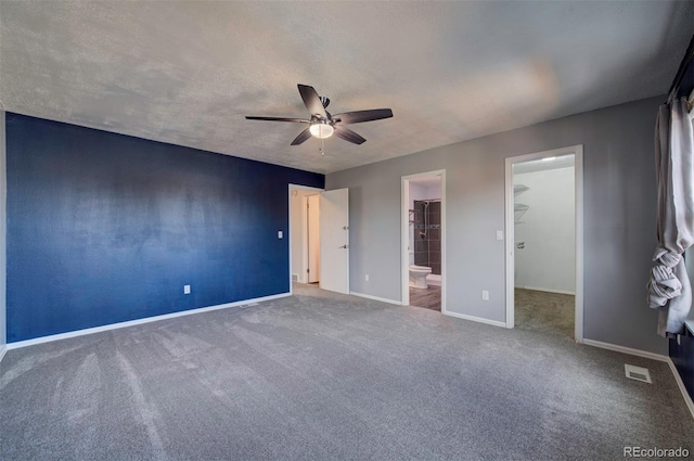 unfurnished bedroom with ceiling fan, carpet flooring, connected bathroom, a textured ceiling, and a spacious closet