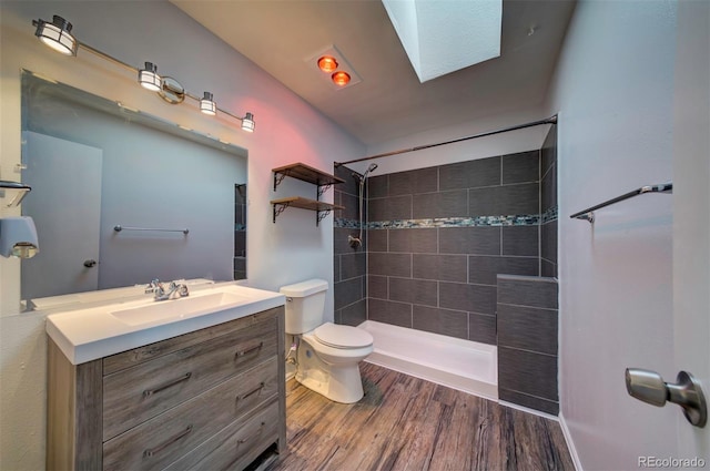 bathroom with hardwood / wood-style floors, a skylight, vanity, a tile shower, and toilet