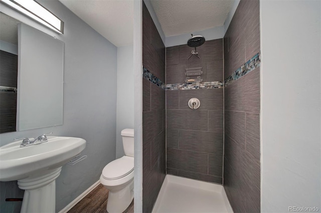 bathroom with a tile shower, a textured ceiling, wood-type flooring, and toilet