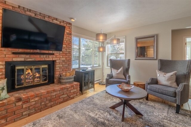 living area with wood finished floors, a brick fireplace, and a baseboard heating unit