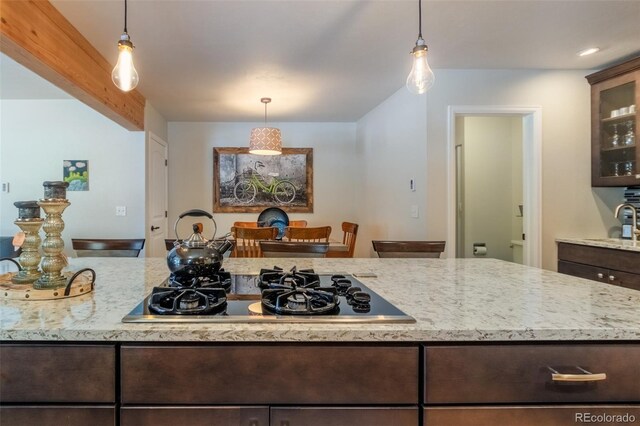 kitchen with dark brown cabinets, black gas cooktop, light stone countertops, glass insert cabinets, and a sink