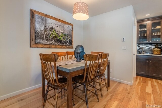 dining space with light wood-type flooring, baseboards, bar area, and recessed lighting