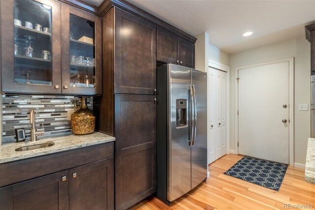 kitchen with stainless steel fridge, a sink, dark brown cabinets, light wood finished floors, and decorative backsplash
