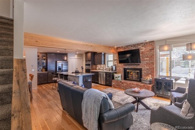 living area with stairway, plenty of natural light, a brick fireplace, and light wood-style floors