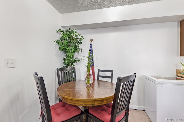 dining space with a textured ceiling, washer and clothes dryer, and light colored carpet