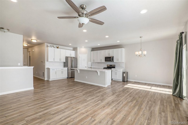 kitchen featuring appliances with stainless steel finishes, hanging light fixtures, white cabinets, ceiling fan with notable chandelier, and light wood-type flooring