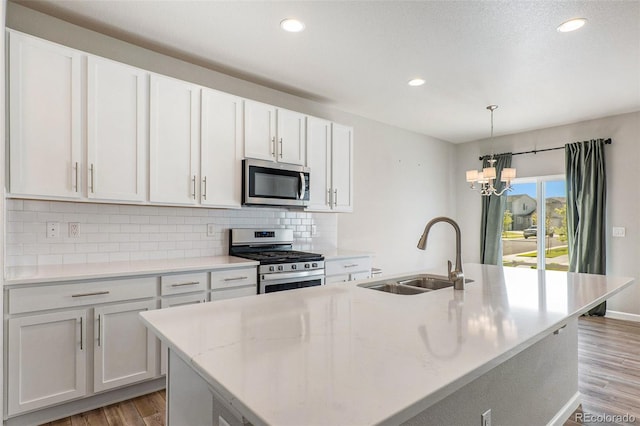 kitchen featuring appliances with stainless steel finishes, decorative light fixtures, an island with sink, sink, and white cabinets