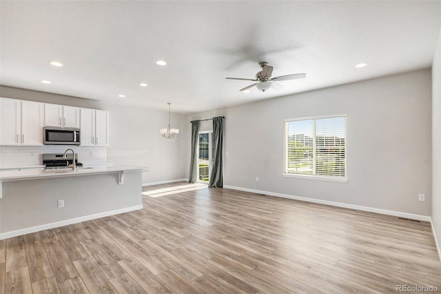 kitchen with white cabinetry, light hardwood / wood-style flooring, hanging light fixtures, appliances with stainless steel finishes, and backsplash