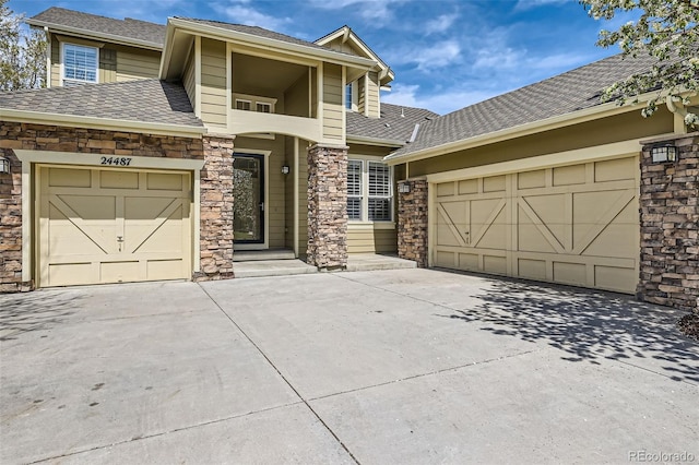 view of front facade with roof with shingles, driveway, stone siding, and a garage