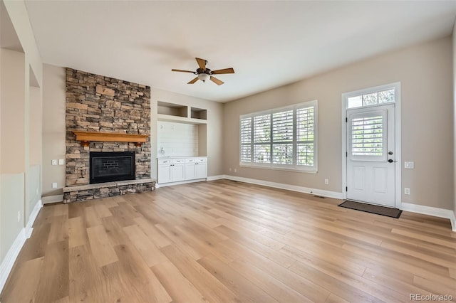 unfurnished living room featuring ceiling fan, a fireplace, built in shelves, baseboards, and light wood finished floors