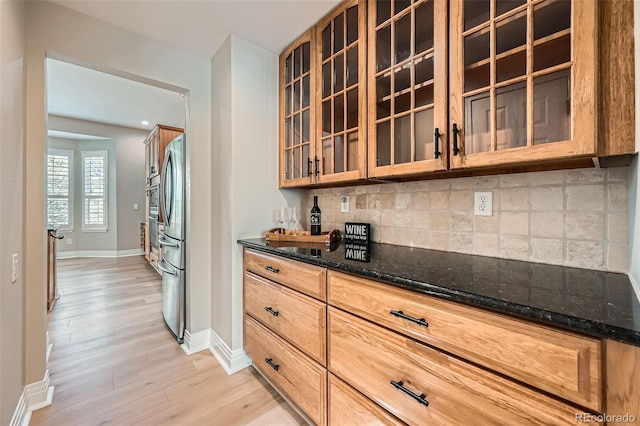 bar featuring decorative backsplash, light wood-type flooring, baseboards, a bar, and freestanding refrigerator