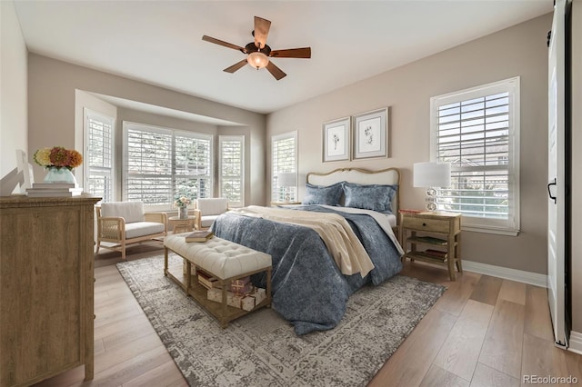 bedroom with baseboards, multiple windows, a ceiling fan, and light wood finished floors
