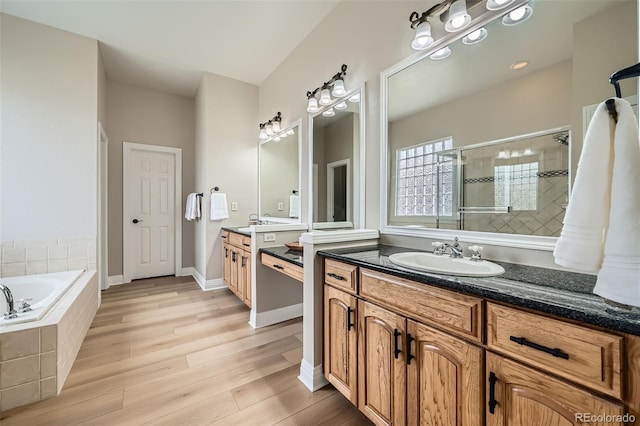 full bathroom with a garden tub, wood finished floors, two vanities, a sink, and a stall shower