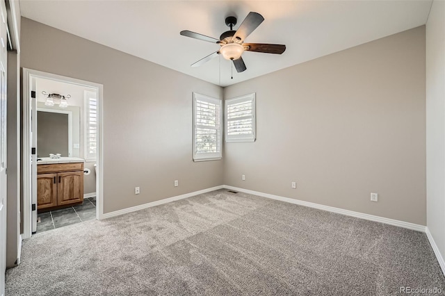 unfurnished bedroom with a ceiling fan, baseboards, light carpet, and ensuite bath