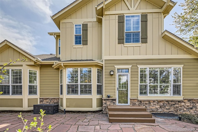 back of property featuring board and batten siding, a patio, stone siding, and roof with shingles