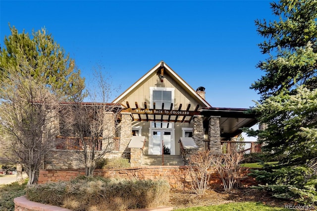 back of property with board and batten siding, a chimney, and stone siding