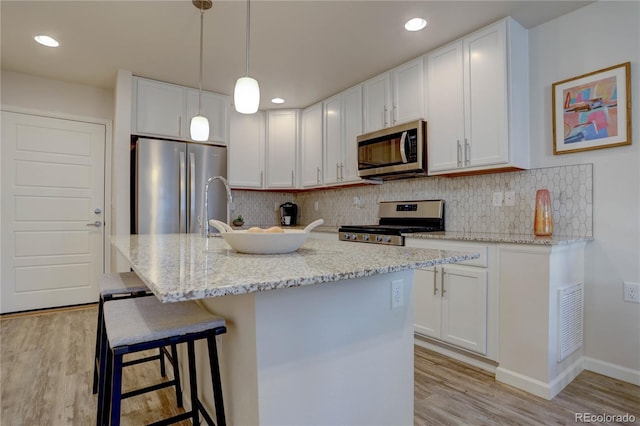 kitchen with pendant lighting, backsplash, an island with sink, appliances with stainless steel finishes, and white cabinetry