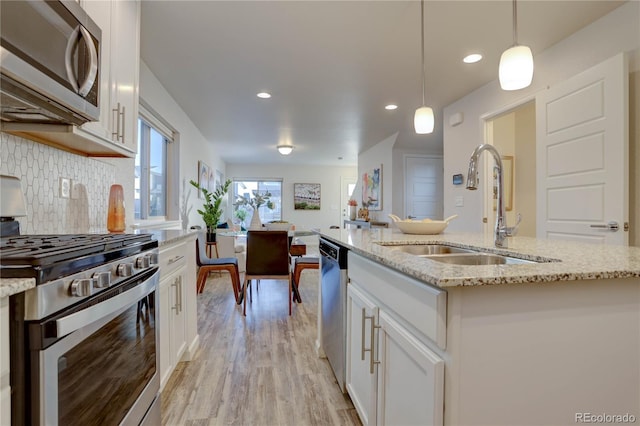 kitchen featuring a kitchen island with sink, hanging light fixtures, white cabinets, and stainless steel appliances