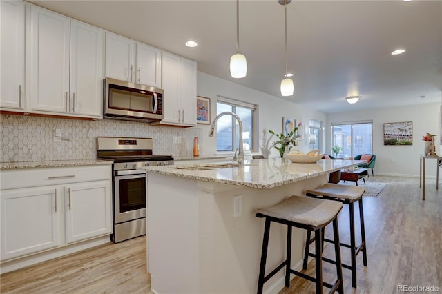 kitchen featuring white cabinets, decorative light fixtures, stainless steel appliances, and a center island with sink