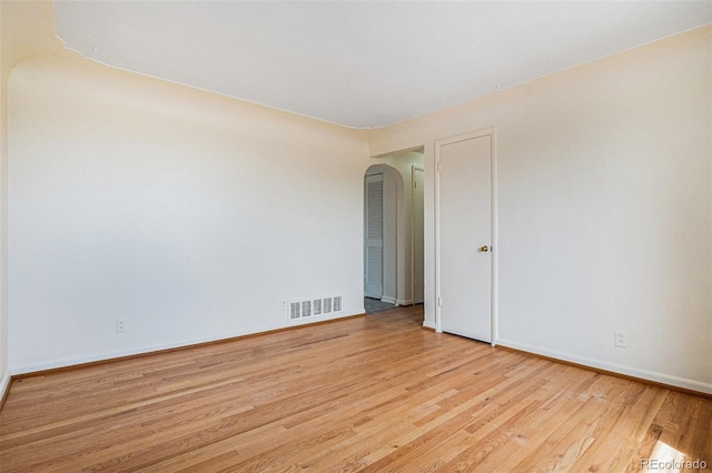 empty room featuring wood finished floors, arched walkways, baseboards, and visible vents