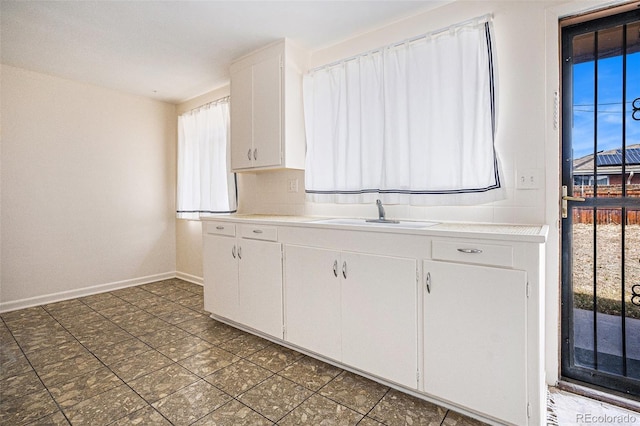 kitchen with a sink, baseboards, white cabinetry, and light countertops