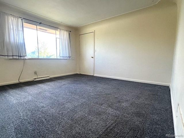 spare room featuring dark carpet, a baseboard heating unit, and baseboards
