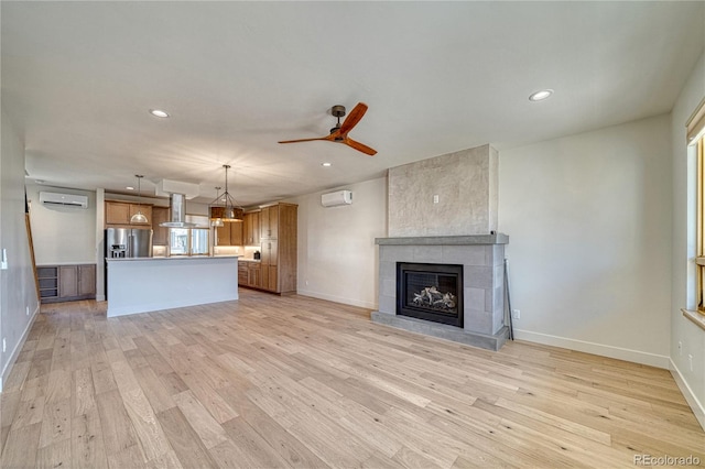 unfurnished living room featuring a ceiling fan, a tiled fireplace, a wall unit AC, recessed lighting, and light wood finished floors