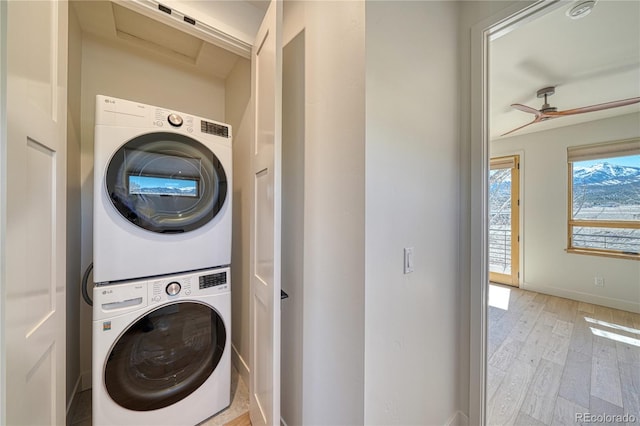 laundry room featuring baseboards, laundry area, ceiling fan, light wood-style floors, and stacked washer / dryer