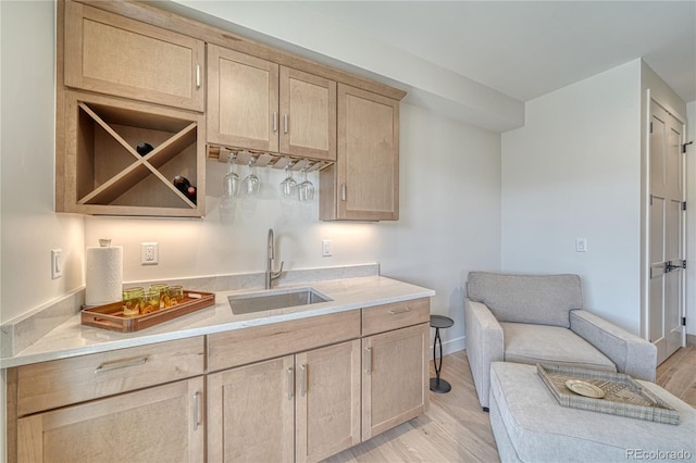 kitchen featuring a sink, baseboards, light wood-style flooring, and light brown cabinets