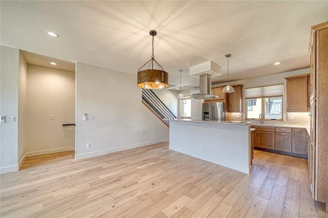 kitchen with pendant lighting, light wood-style flooring, high quality fridge, island range hood, and a sink