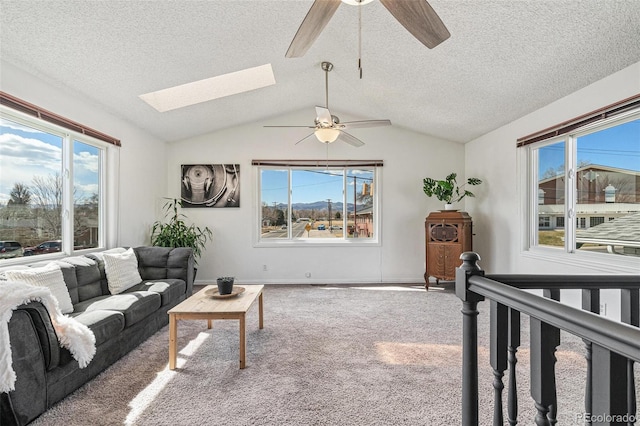 carpeted living area with vaulted ceiling with skylight, a textured ceiling, and ceiling fan