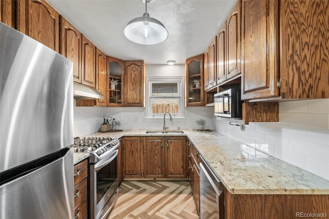 kitchen with a sink, stainless steel appliances, under cabinet range hood, and brown cabinetry