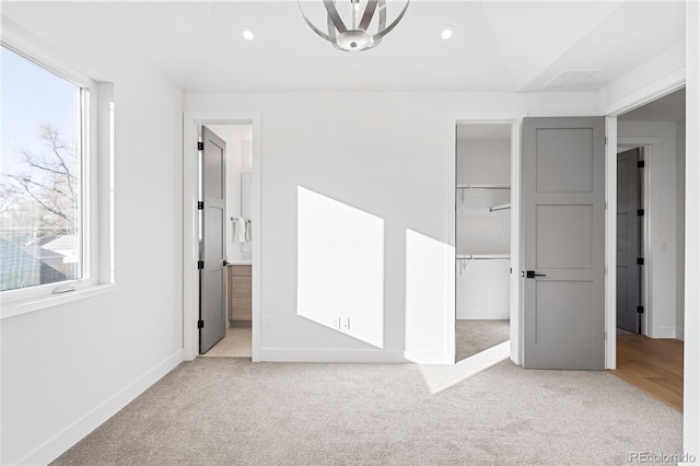 unfurnished bedroom featuring ensuite bathroom, a spacious closet, multiple windows, and light colored carpet