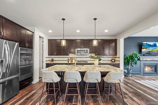 kitchen featuring a kitchen bar, stainless steel appliances, hanging light fixtures, an island with sink, and dark brown cabinets