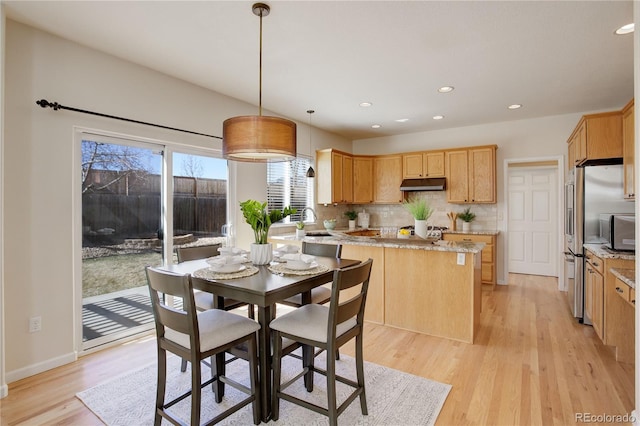 kitchen featuring light wood finished floors, backsplash, light brown cabinets, under cabinet range hood, and a sink