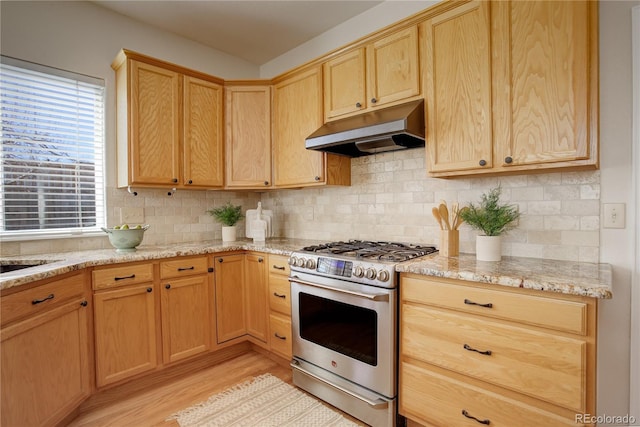 kitchen with light brown cabinets, stainless steel range with gas stovetop, decorative backsplash, light wood-style floors, and under cabinet range hood