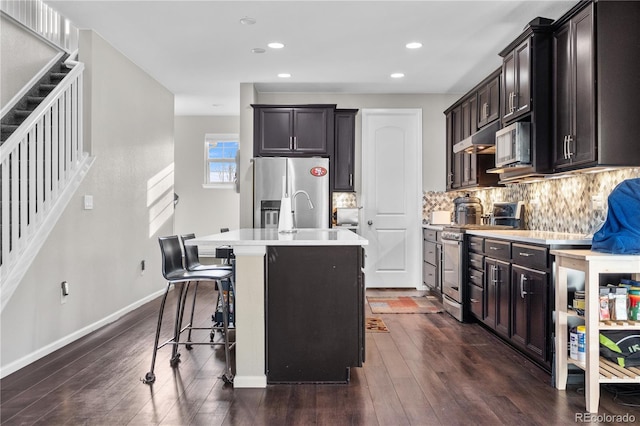 kitchen featuring sink, stainless steel appliances, dark hardwood / wood-style flooring, a kitchen island with sink, and a breakfast bar