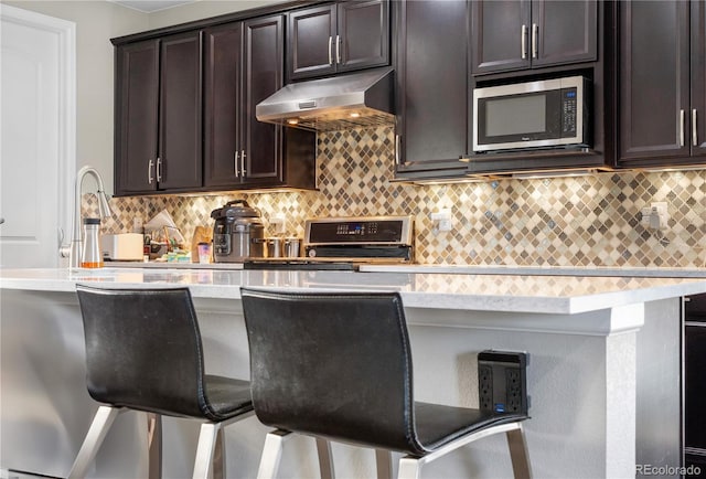 kitchen with decorative backsplash, a kitchen bar, dark brown cabinetry, and stainless steel appliances