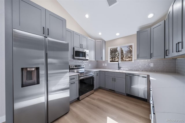 kitchen featuring appliances with stainless steel finishes, lofted ceiling, sink, gray cabinetry, and light hardwood / wood-style flooring