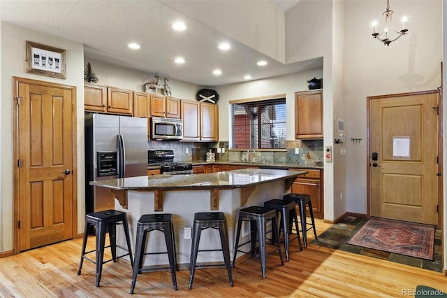 kitchen with light wood finished floors, tasteful backsplash, appliances with stainless steel finishes, a breakfast bar, and a center island