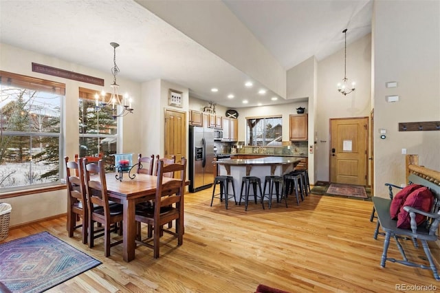 dining room with light wood-type flooring, high vaulted ceiling, a notable chandelier, and recessed lighting