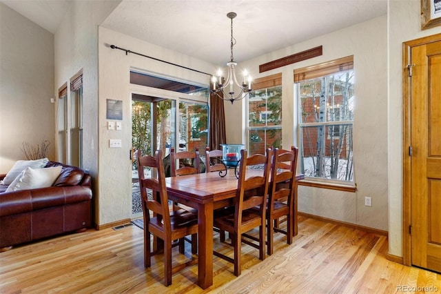 dining room with light wood-style floors, baseboards, a chandelier, and a textured wall