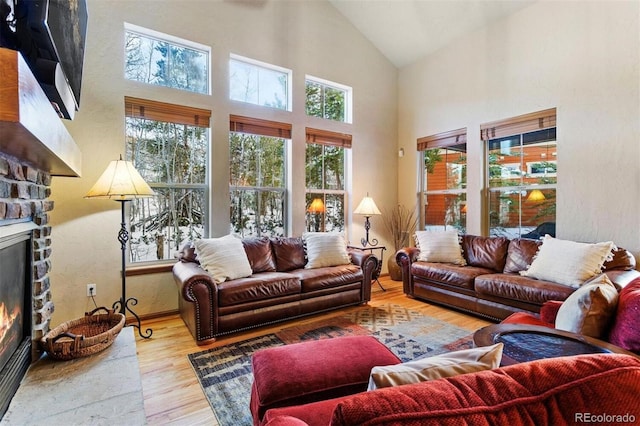 living room with high vaulted ceiling, a wealth of natural light, a stone fireplace, and wood finished floors