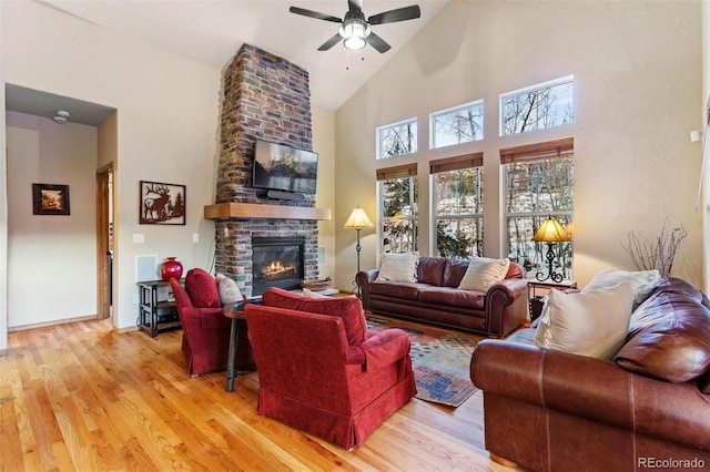 living area featuring ceiling fan, a stone fireplace, wood finished floors, high vaulted ceiling, and baseboards