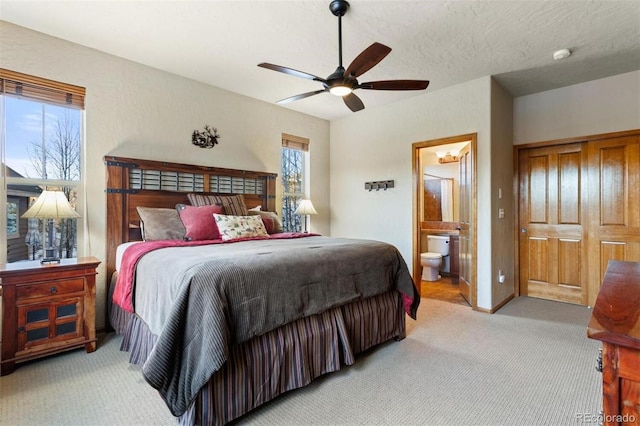 bedroom with a textured ceiling, ceiling fan, ensuite bath, and light colored carpet