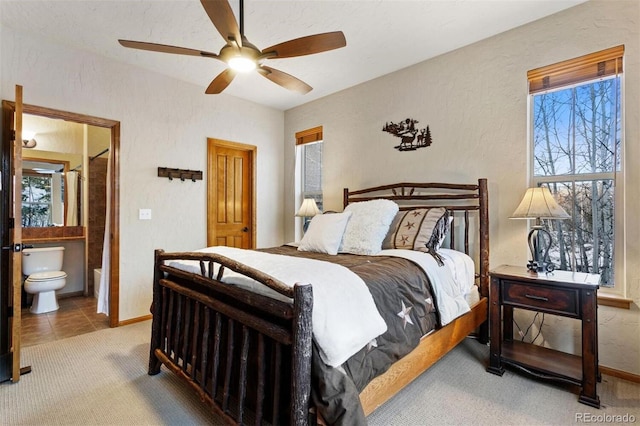 carpeted bedroom featuring ensuite bath, baseboards, a ceiling fan, and a textured wall