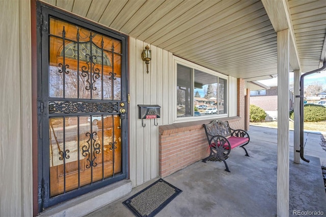 view of exterior entry featuring a porch and brick siding