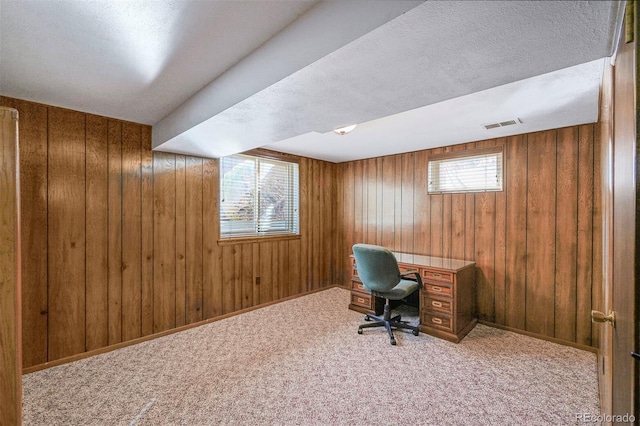 carpeted office space with baseboards, wooden walls, visible vents, and a textured ceiling