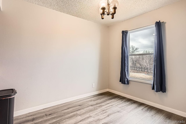 unfurnished room with a textured ceiling, light hardwood / wood-style flooring, and a notable chandelier