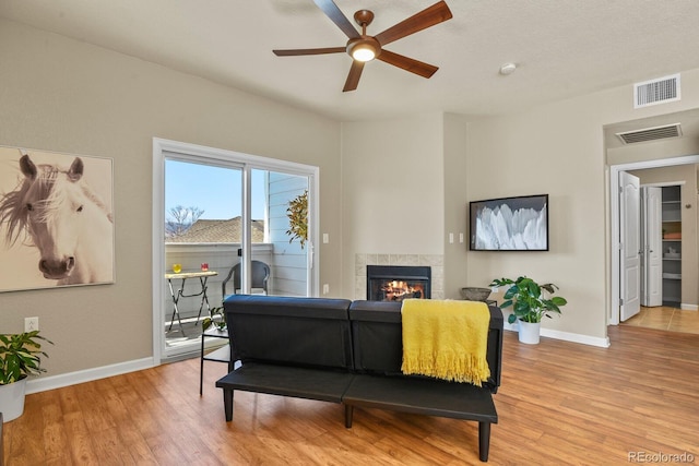 living room featuring a tiled fireplace, ceiling fan, and light wood-type flooring